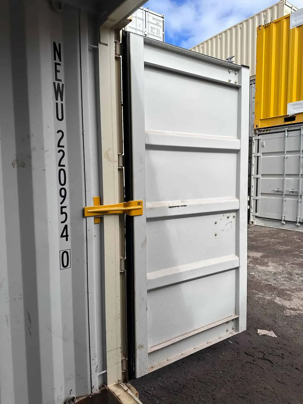 A container door braced open at 90 degrees, seen from outside in a container yard